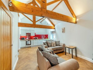 A spacious living area with a high ceiling and exposed wooden beams, a modern kitchen with red accents, and a cozy seating area with a sofa and ottoman. - A lovely 1st floor apartment with views towards the open fields. (Low Hunsley, Cottingham)