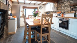 Een rustieke keuken met zichtbare houten balken, stenen muren en een eethoek met een houten tafel en stoelen.