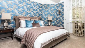 Een slaapkamer met een groot bed, twee nachtkastjes, een decoratieve wand en een raam met jaloezieën.