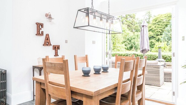 Een eetgedeelte met een houten tafel en stoelen, een hanglamp en uitzicht op het omliggende landschap.