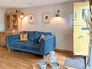 A cozy living room with a blue sofa, wooden cabinet, and framed pictures on the wall. - 2 bedroom accommodation in Stiffkey (Stiffkey)