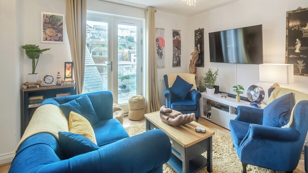 Una sala de estar moderna con sofás azules, una mesa de centro de madera y un televisor montado en la pared.