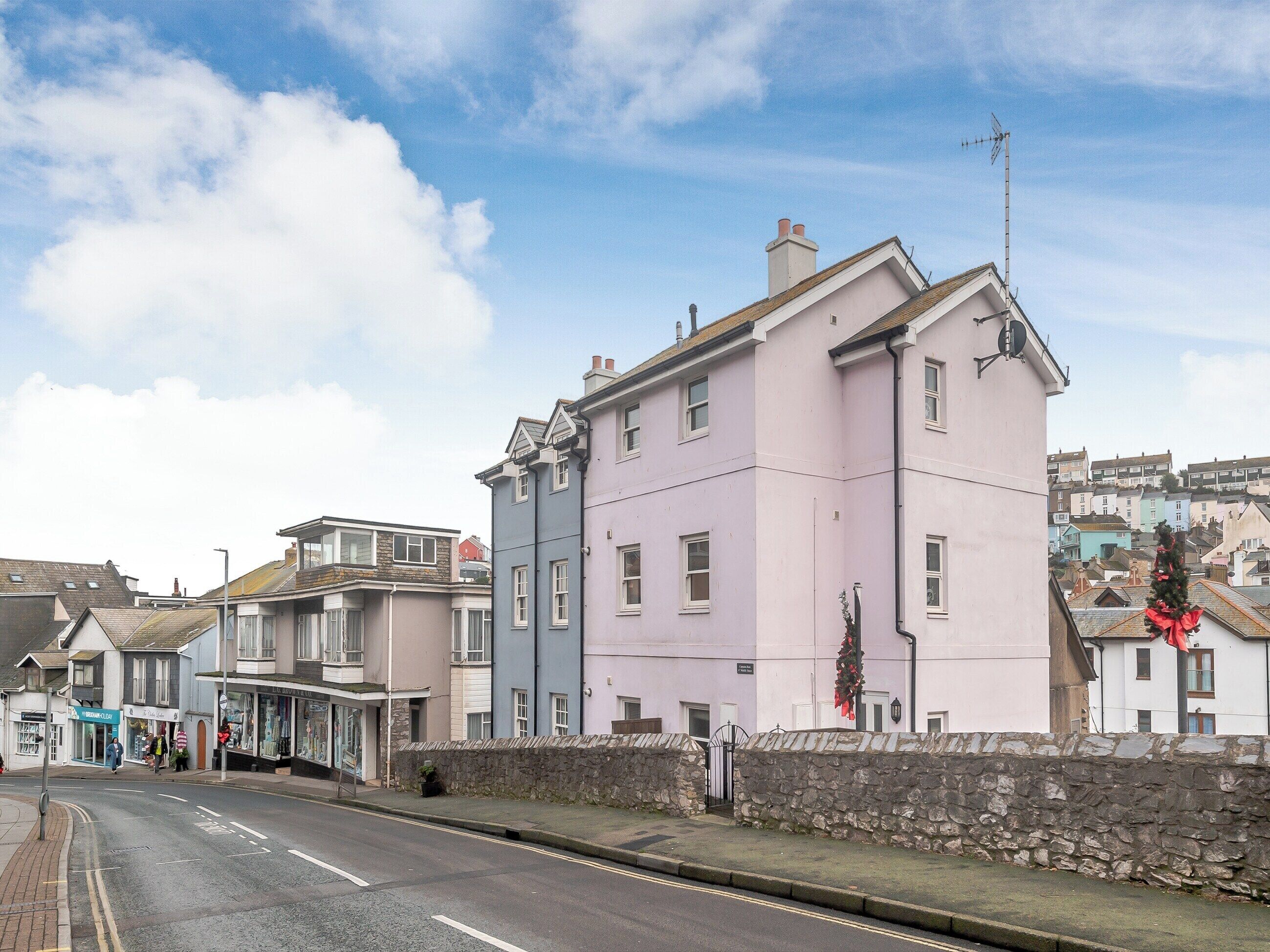 A street view with a row of multi-story buildings, including a pink building with a stone wall in front.