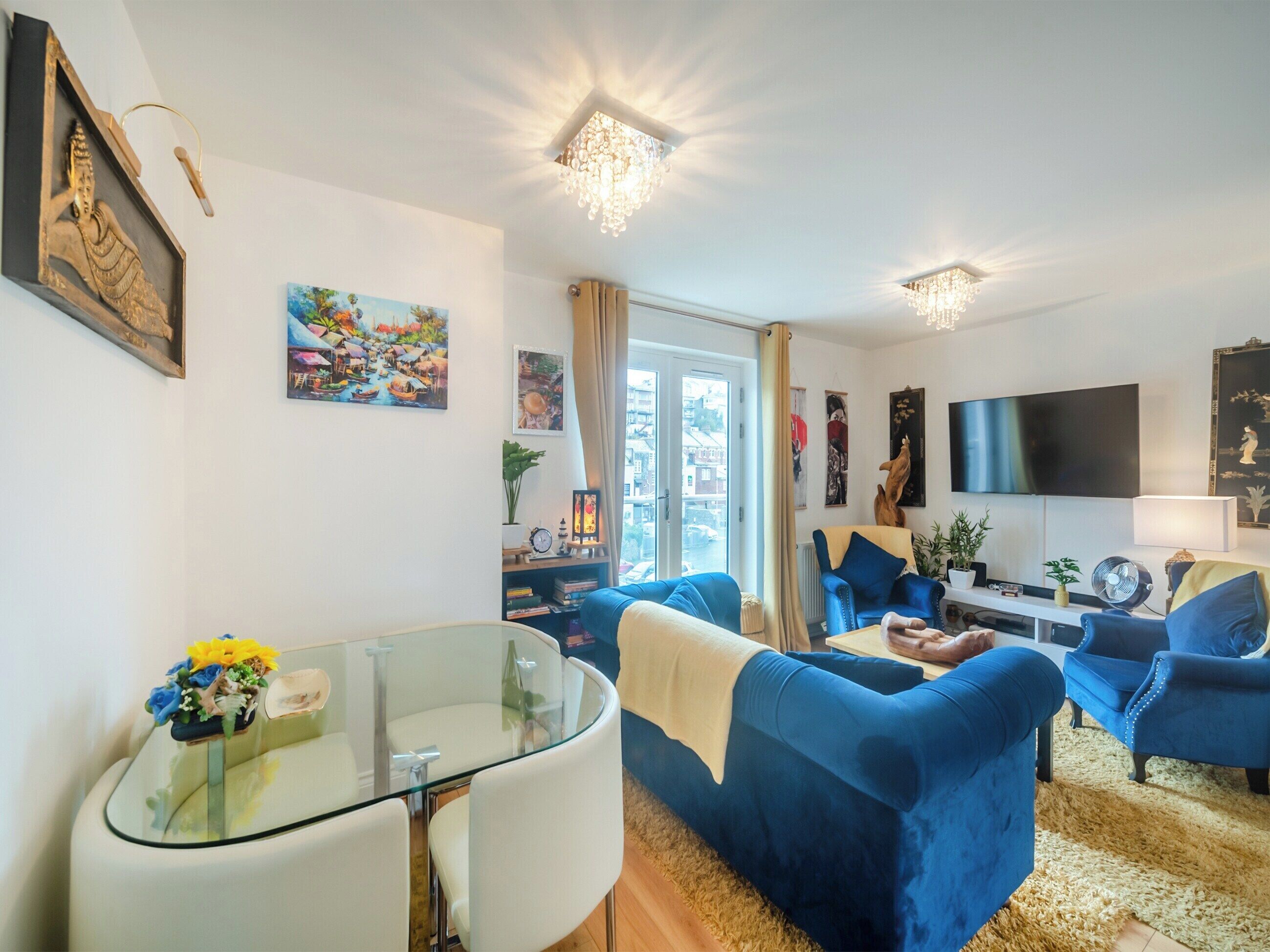Ein modernes Wohnzimmer mit einem Glastisch, blauen Sofas und einem Flachbildfernseher.