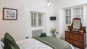 Une chambre à coucher avec un lit, une commode, un radiateur, un téléviseur et une fenêtre avec des volets.