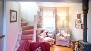 A cozy living room with a fireplace, a staircase, and a view of the outdoors. - A cute and characterful cottage in a charming coastal port. (Blakeney)