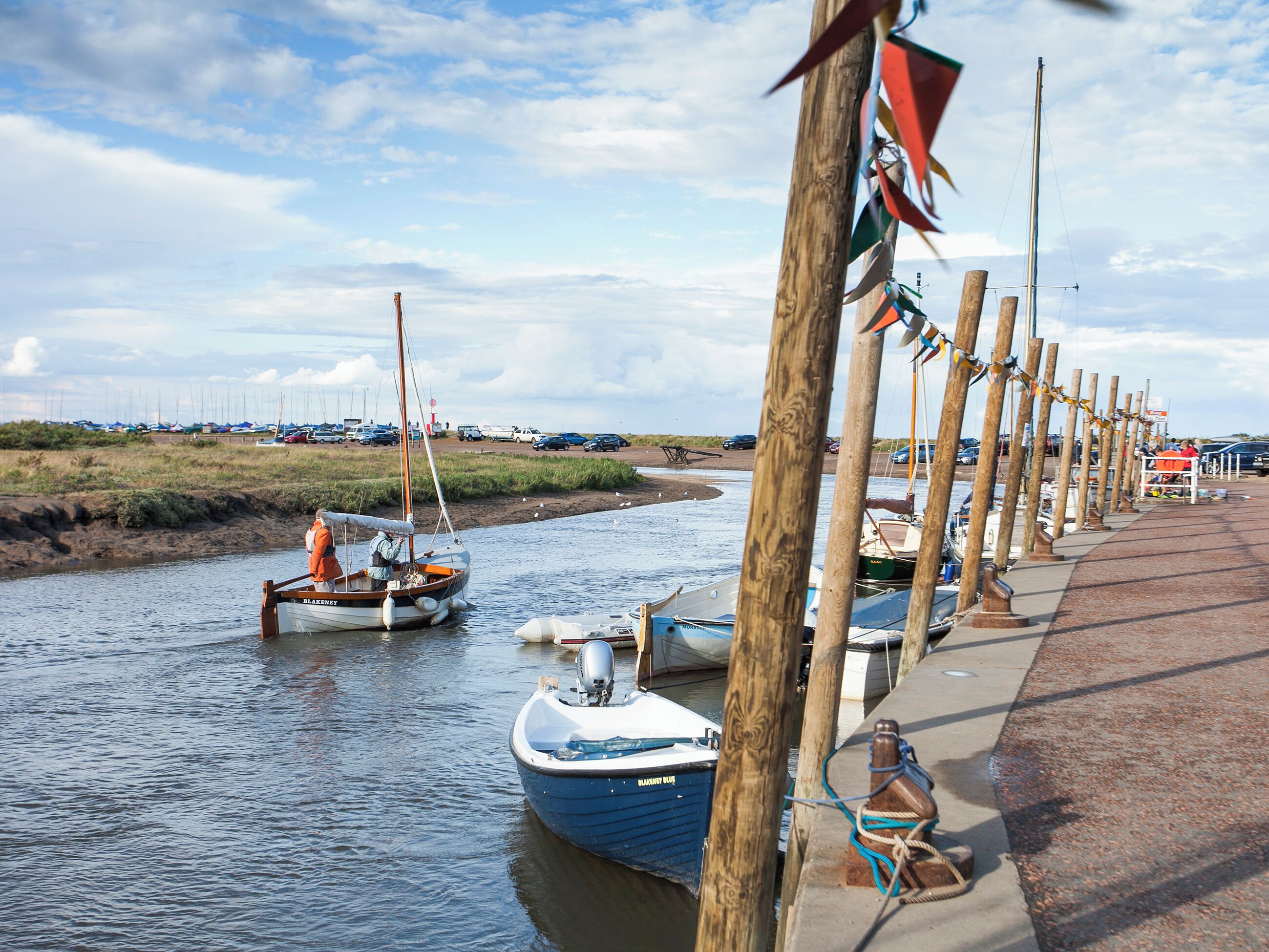 Een steiger aan de rivier met boten, een houten looppad en een grasveld op de achtergrond.