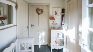 A hallway with a white door, a heart-shaped wreath, a small cabinet with drawers, and a chair. - A cute and characterful cottage in a charming coastal port. (Blakeney)