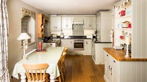 A kitchen with white cabinets, a wooden dining table, and a central island. - A cute and characterful cottage in a charming coastal port. (Blakeney)