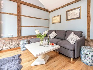 A cozy living room with a grey sofa, a white coffee table, and a brick wall. - 1 bedroom accommodation in Hacheston, near Wickham Market (Hacheston, near Wickham Market)