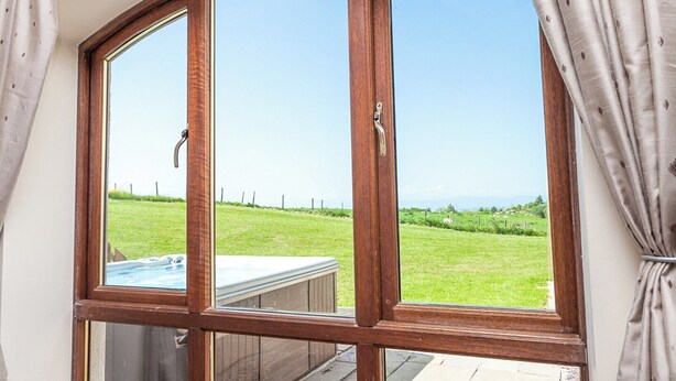 A large arched window with a view of a grassy yard and a hot tub.