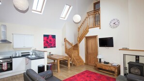 Ein geräumiger Wohnbereich mit Küche, einem Esstisch, einer Couch, einem Kamin und einer Treppe.