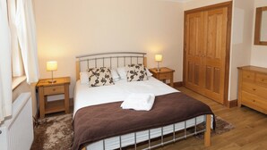 Ein Schlafzimmer mit einem Bett, zwei Nachttischen, einem Holzschrank und einem Fenster mit Vorhängen.