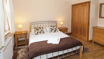 A bedroom with a bed, two bedside tables, a wooden wardrobe, and a window with curtains.