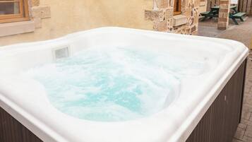 A hot tub in an outdoor setting with stone walls and wooden furniture.