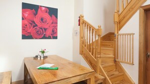 En trätrappa med ett räcke, ett träbord med en vas med blommor och en målning av röda rosor på väggen.