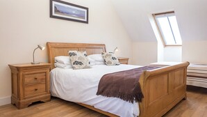 Ein Schlafzimmer mit einem hölzernen Bett, zwei Nachttischen, einem Beistelltisch, einem gerahmten Bild an der Wand und einem Oberlicht.