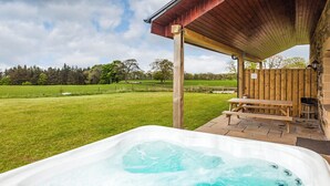 Ein Whirlpool mit Holzterrasse und Sitzbank, umgeben von einer Wiese und Bäumen.