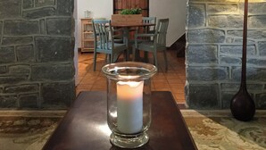 A candle in a glass holder on a table, a wooden dining table with chairs, a clock on the wall, and a stone wall. - 2 bedroom accommodation in Over Haddon, near Bakewell (Over Haddon, near Bakewell)