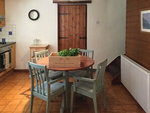 Un coin repas avec une table et des chaises en bois, une horloge au mur et une porte en bois.