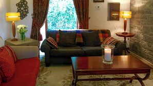 A cozy living room with a sofa, a coffee table, and two lamps. There is a window with curtains, a wall clock, and a framed picture. - 2 bedroom accommodation in Over Haddon, near Bakewell (Over Haddon, near Bakewell)