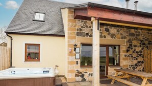 Ein Haus mit Natursteinaußenwand, einer Holzterrasse, einem Whirlpool und einem Holztisch mit Bänken.
