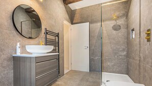 Un bany modern amb una banyera gran, un mirall rodó, un lavabo blanc i una zona de banyera amb portes de vidre.