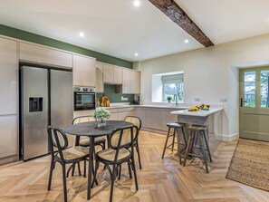 Eine moderne Küche mit Essbereich, ausgestattet mit Kühlschrank, Backofen und Barhocker.