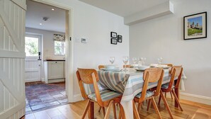 Ein Essbereich mit einem Holztisch, gedeckt für vier Personen, umgeben von gestreiften Stühlen. Im Hintergrund ist eine Küche erkennbar, und ein gerahmtes Bild hängt an der Wand.