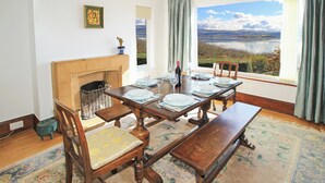 Comedor con una mesa grande dispuesta para seis, chimenea y una vista panorámica de un lago y montañas.