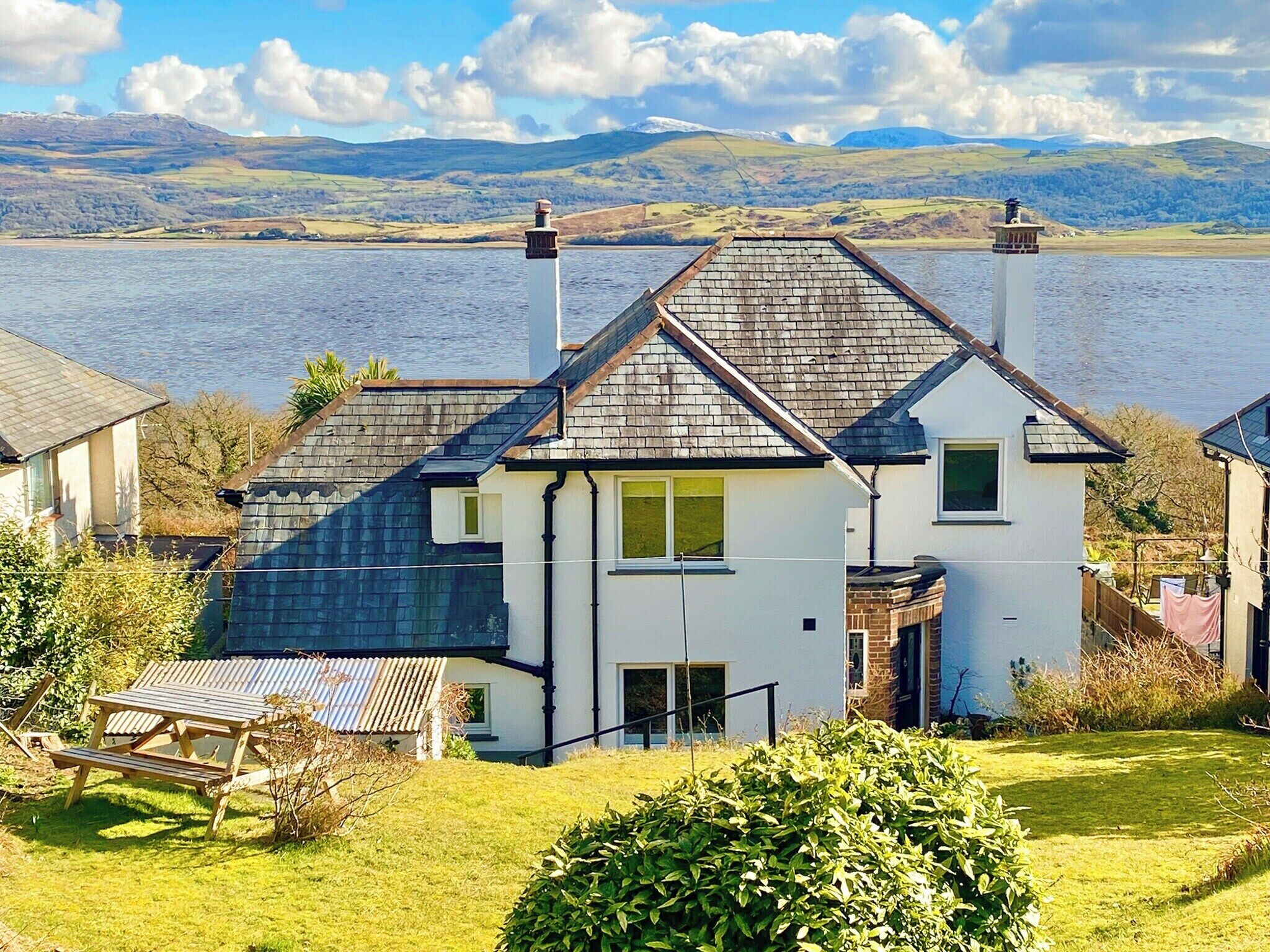 A two-story house with a sloped roof, a chimney, and a view of a lake and mountains in the background.