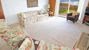 Una sala de estar con sofás de estampado floral, un televisor de pantalla plana y un ventanal con vistas panorámicas.