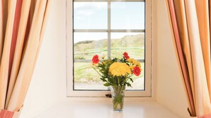 Una finestra con vista su un paesaggio erboso, un vaso con fiori e tende.