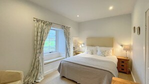 Una camera da letto con un letto, una finestra con tende, un comodino con una lampada e un tavolo di fianco al letto.