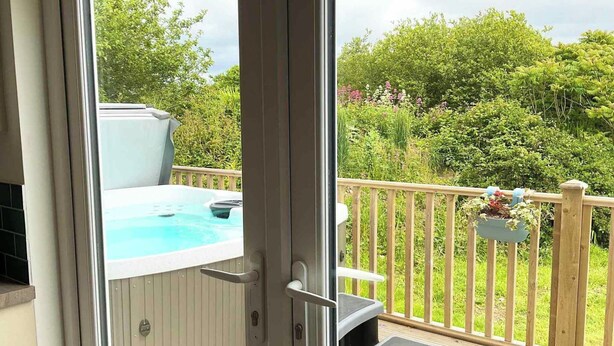 A hot tub on a deck with a wooden railing and a small step leading up to it. - Holywell - CWC610826 (Perranporth)