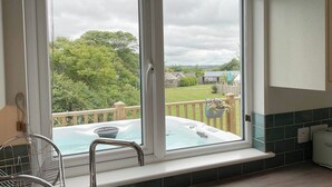 A room with a large window overlooking a garden and a hot tub. - Holywell - CWC610826 (Perranporth)