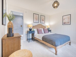 Une chambre à coucher comprenant un lit, des tables de chevet, une lampe, un luminaire fixé au mur et des reproductions botaniques encadrées.