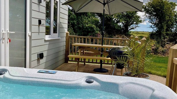 Ein Whirlpool mit Holzterrasse und Sitzbank, umgeben von Grün und blauem Himmel.
