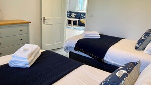 Ein Hotelzimmer mit zwei Betten, einem Holzschrank, einem an der Wand montierten Fernseher und Blick auf den Wohnbereich durch eine offene Tür.