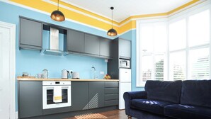 Een moderne keuken met grijze kastjes, een witte oven en een blauw aanrecht. Er is een donkerblauwe bank en een houten vloer met een geometrisch patroon.