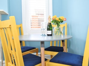 A dining table with a bottle of champagne, a glass, and a vase with flowers. - Bailey Studio Apartment - UKC6337 (Cheltenham)