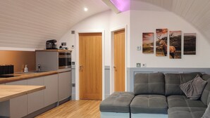 Una cucina moderna con mobili in legno, forno integrato e macchina da caffè. Nell'area soggiorno, un divano grigio con un cuscino decorativo.
