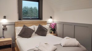Un letto rifatto con due cuscini, una lampada da comodino, un comodino, una finestra con tende e un'orchidea in vaso.