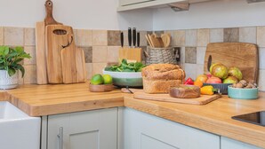 Eine Küche mit Holzarbeitsplatten, einem Schneidebrett, einer Schüssel mit Blattsalat, einem Brotlaib und verschiedenen Früchten und Nüssen.