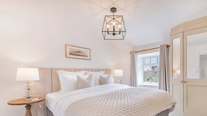 Ein Hotelzimmer mit einem großen Bett, zwei Nachttischen mit Lampen, einer geometrischen Deckenleuchte, einem gerahmten Bild an der Wand und Blick ins Freie durch ein Fenster.