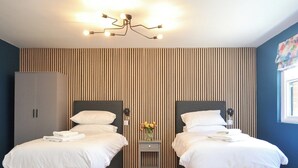 Ein Doppelzimmer mit zwei Betten, einem Schrank, einem Nachttisch mit Blumenvase und einer Deckenleuchte.