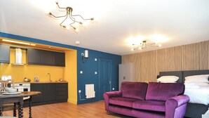 Eine moderne Wohnung mit Küche, einem violetten Sofa und einem Bett mit weißer Bettwäsche.