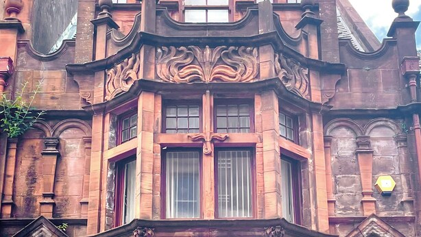 Ein Eckgebäude mit aufwendigen architektonischen Details, großen Fenstern und einer markanten Eingangstür.