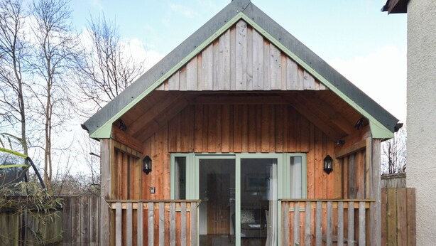 Een houten chalet met een groen dak, een veranda met een leuning en een schuifdeur.'