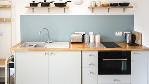 Een moderne keuken met een spoelbak, vaatwasser en oven. Boven het aanrecht staan houten planken met pannen en kommen.